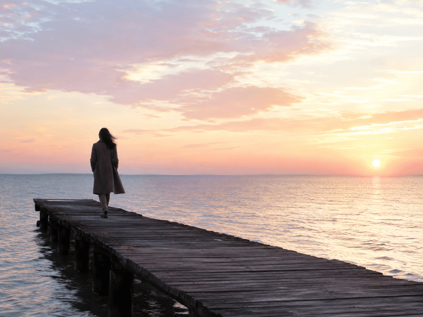 Personne avançant seule vers un horizon apaisé au coucher du soleil.